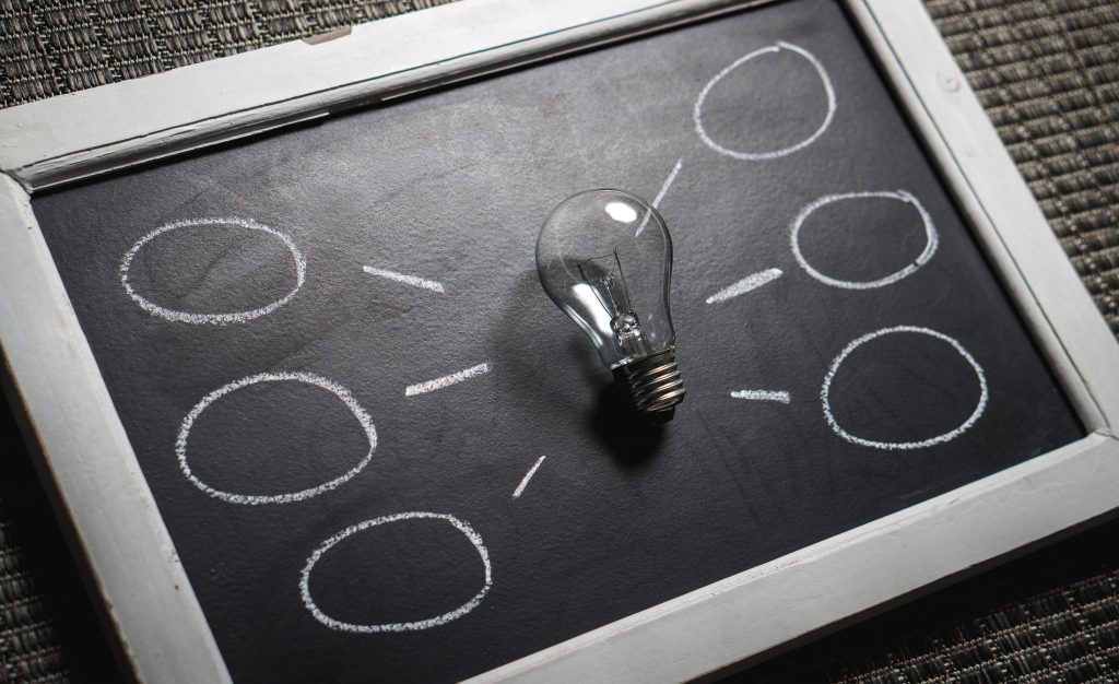 a blackboard with a glass lightbulb in the centre, in the areas around it are 3 thought bubbles chalked on the right and another set on the left