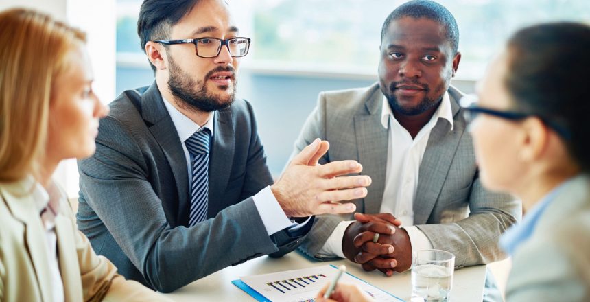 A well-dressed group of 4 discuss a deal around a meeting table - deal or no-deal article